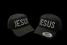 Load image into Gallery viewer, Two black baseball caps with the word 'JESUS' written on them in a stylized font. One cap is positioned with the brim facing up, and the other with the brim facing down.